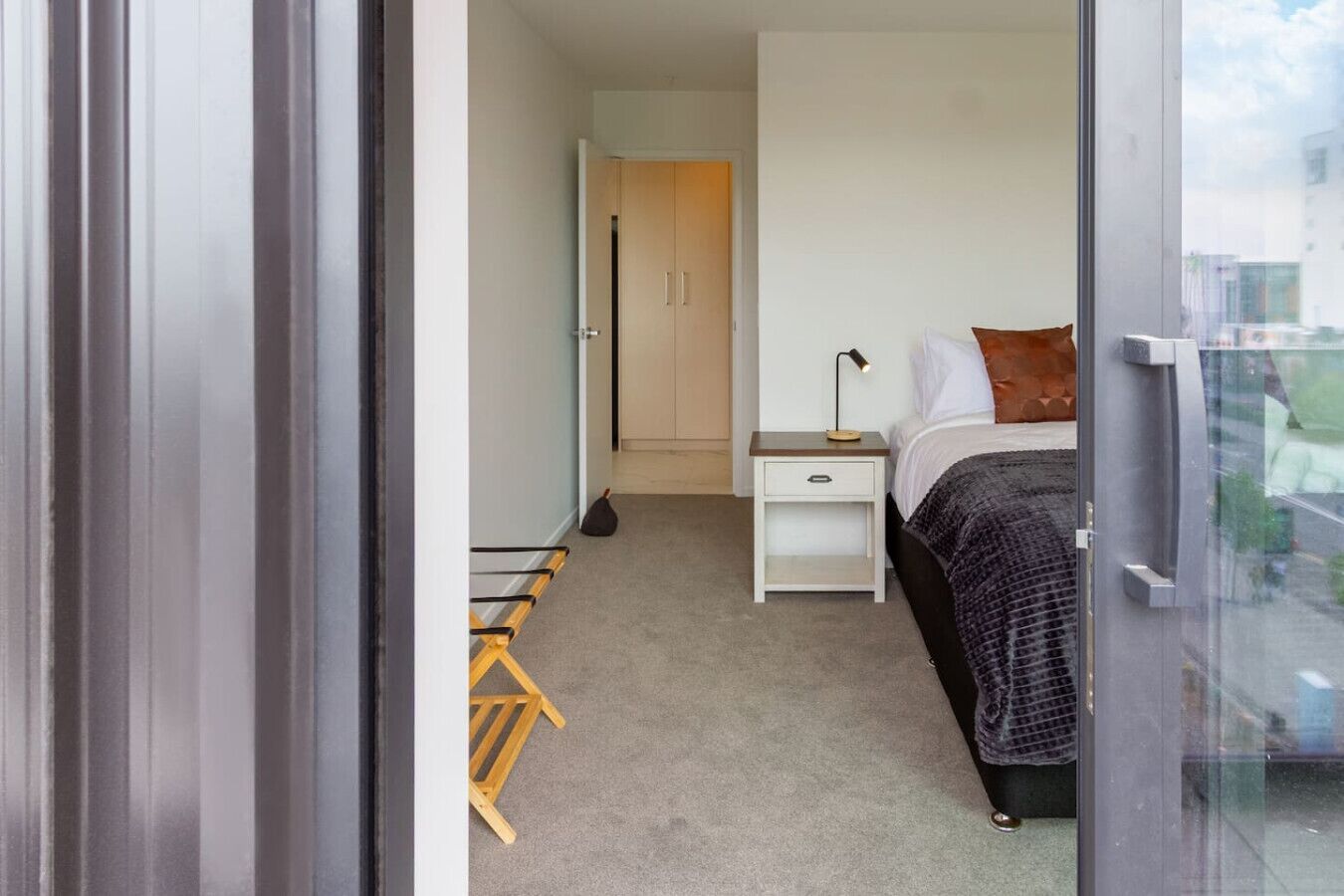 A bedroom with a bed, bedside table, lamp, and a window with a view.