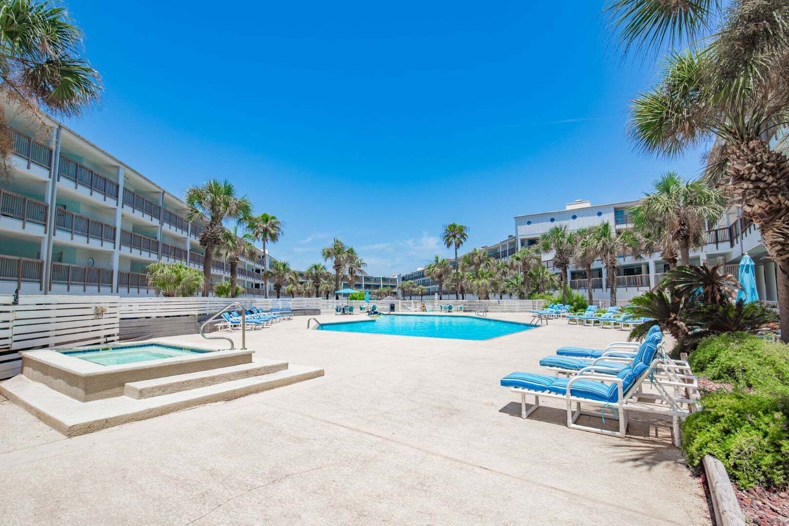 A hotel pool area with multiple lounge chairs, a small pool, and palm trees.