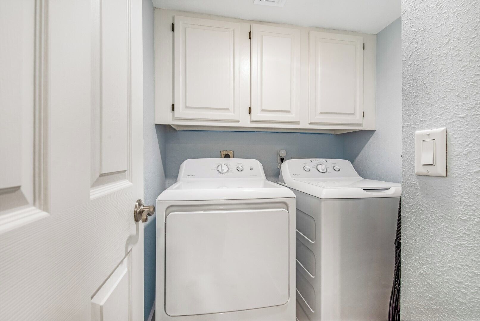 A laundry room with two white front-loading washing machines and a white cabinet above them.