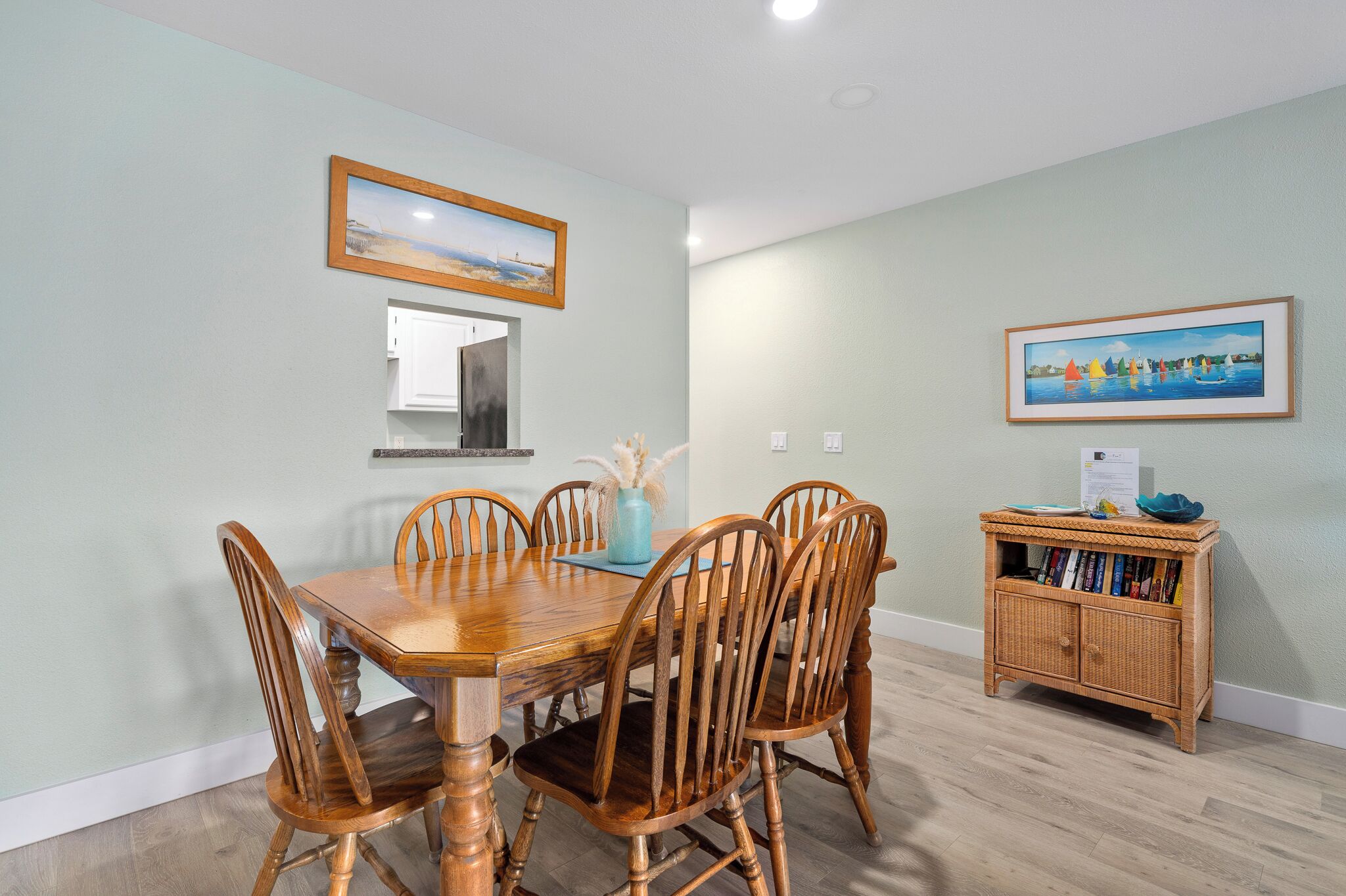 A dining area with a wooden table and chairs, a small side table with a vase, and a bookshelf against the wall.