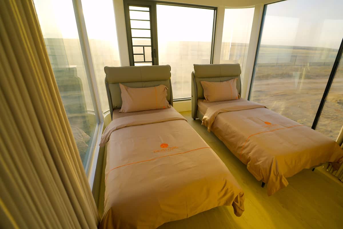 Habitación de hotel con dos camas, ventanas amplias y vistas a la ciudad.
