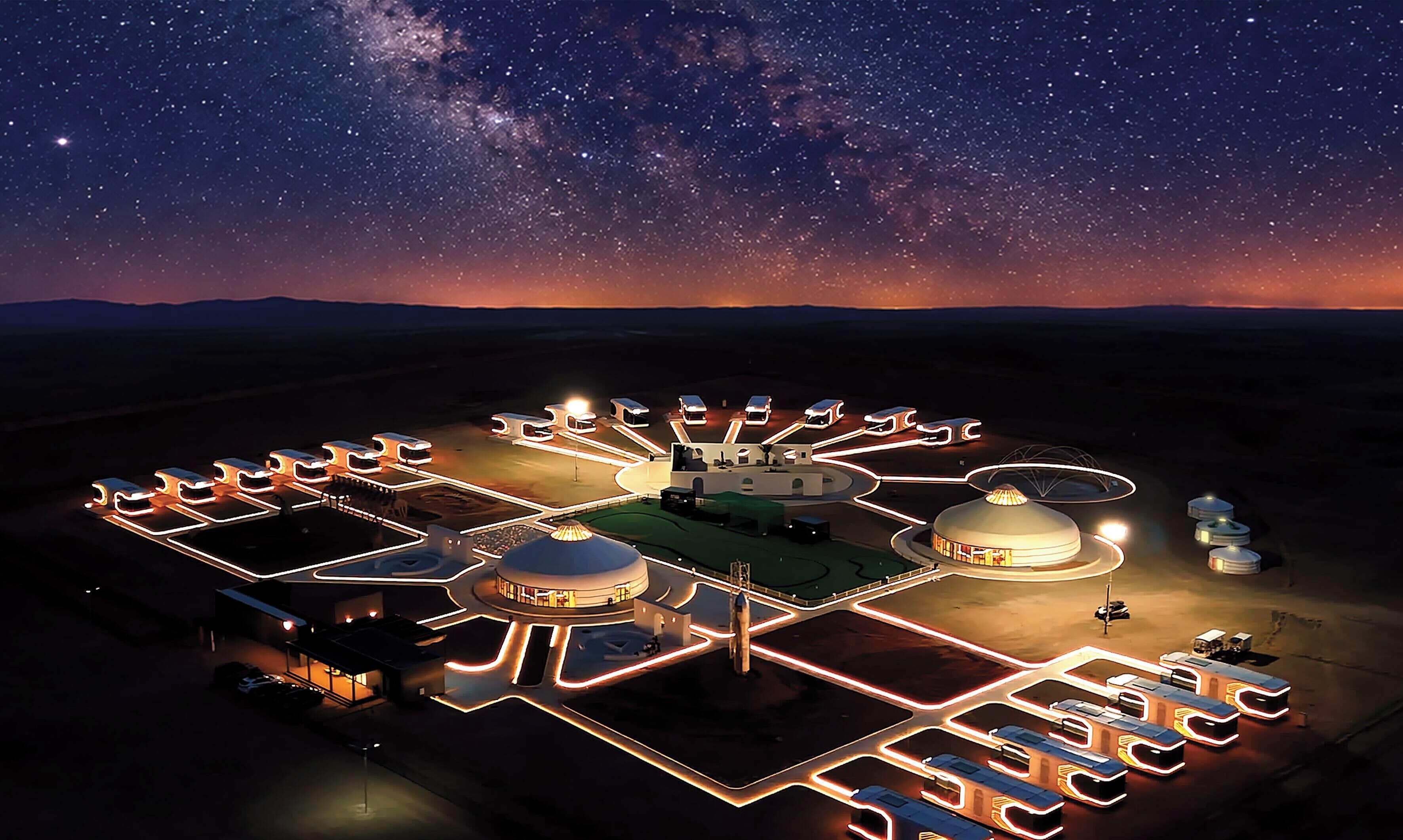 Céu estrelado sobre um resort bem iluminado com várias yurtas e um edifício central.