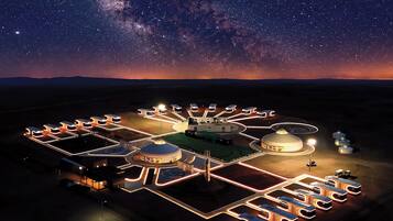 Céu estrelado sobre um resort bem iluminado com várias yurtas e um edifício central.