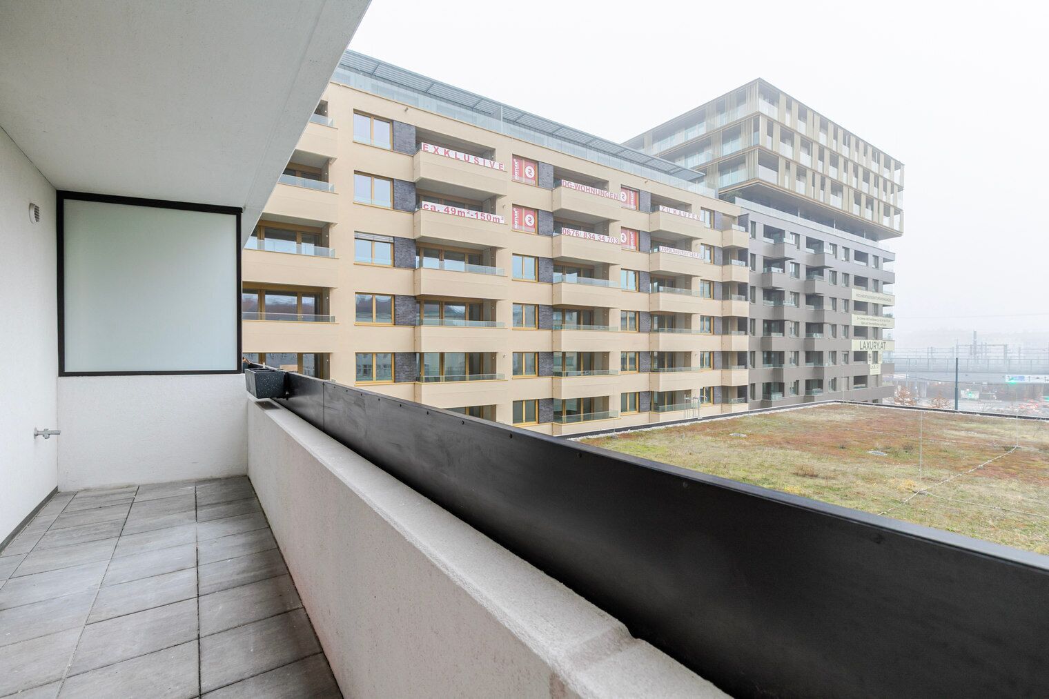 Ein Balkon mit Blick auf ein mehrstöckiges Gebäude, das Balkone und eine Glasfassade zeigt.