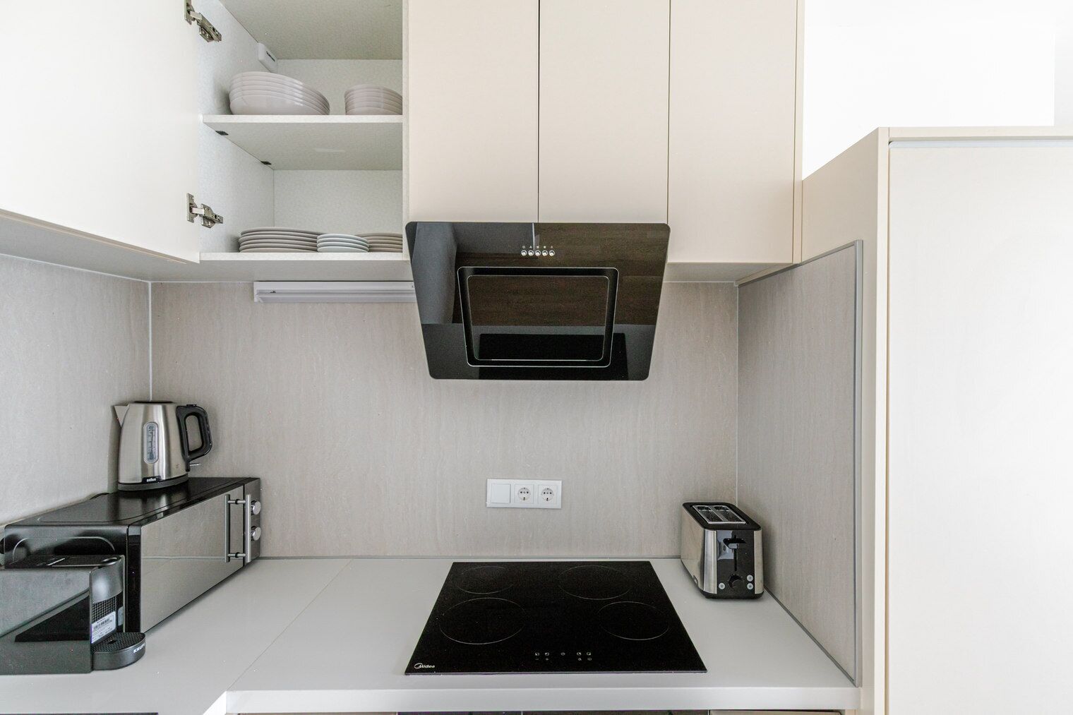 A compact kitchen with a built-in stove, a toaster, and a kettle on the countertop.