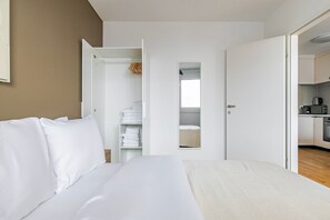 Una habitación de hotel con una cama, un armario con ropa colgada y vistas a la cocina.