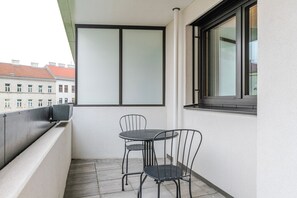 A balcony with a table and two chairs, a window, and a view of buildings in the background. - Blueground | Favoriten, jacuzzi, nr Belvedere (Vienna)