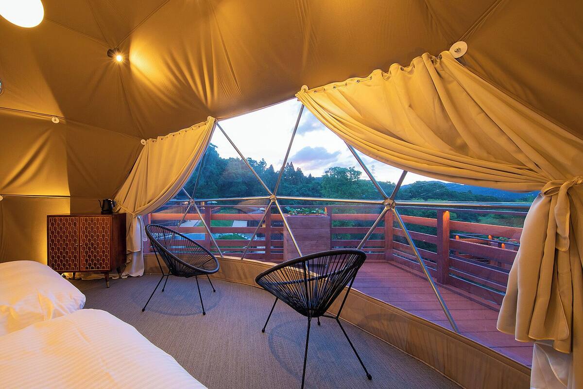 Een slaapkamer met een bed, twee stoelen, een kledingkast en uitzicht op een brug en groen.