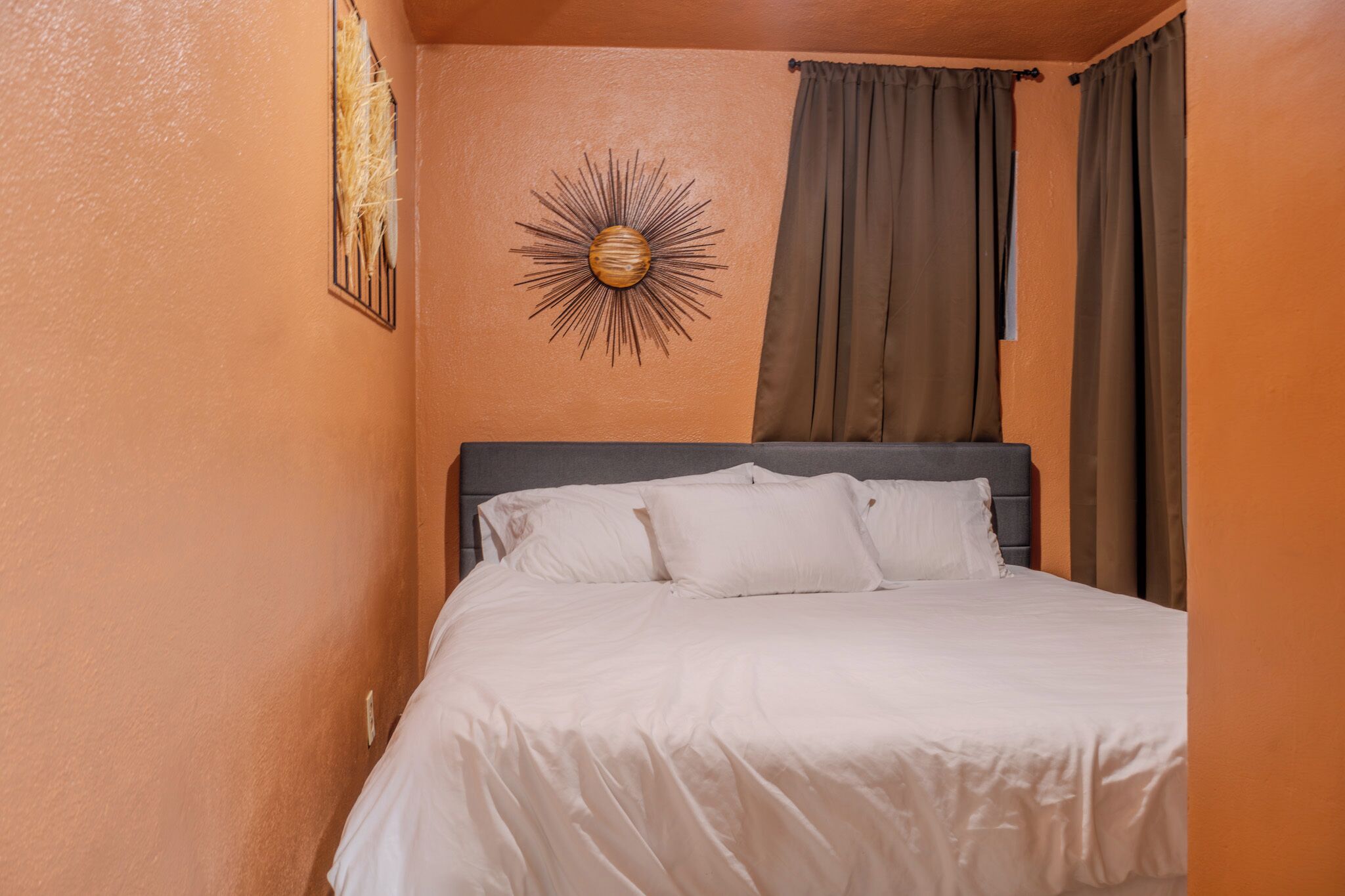 Une chambre à coucher avec un lit, une tête de lit, une décoration murale en forme de soleil et une fenêtre avec des rideaux.