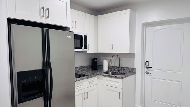 Una cocina compacta con armarios blancos, un refrigerador de acero inoxidable, un microondas, un fregadero y una puerta con picaporte.