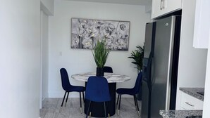 Una cocina moderna con un refrigerador de acero inoxidable, encimera de mármol y un comedor con mesa redonda y sillas azules.