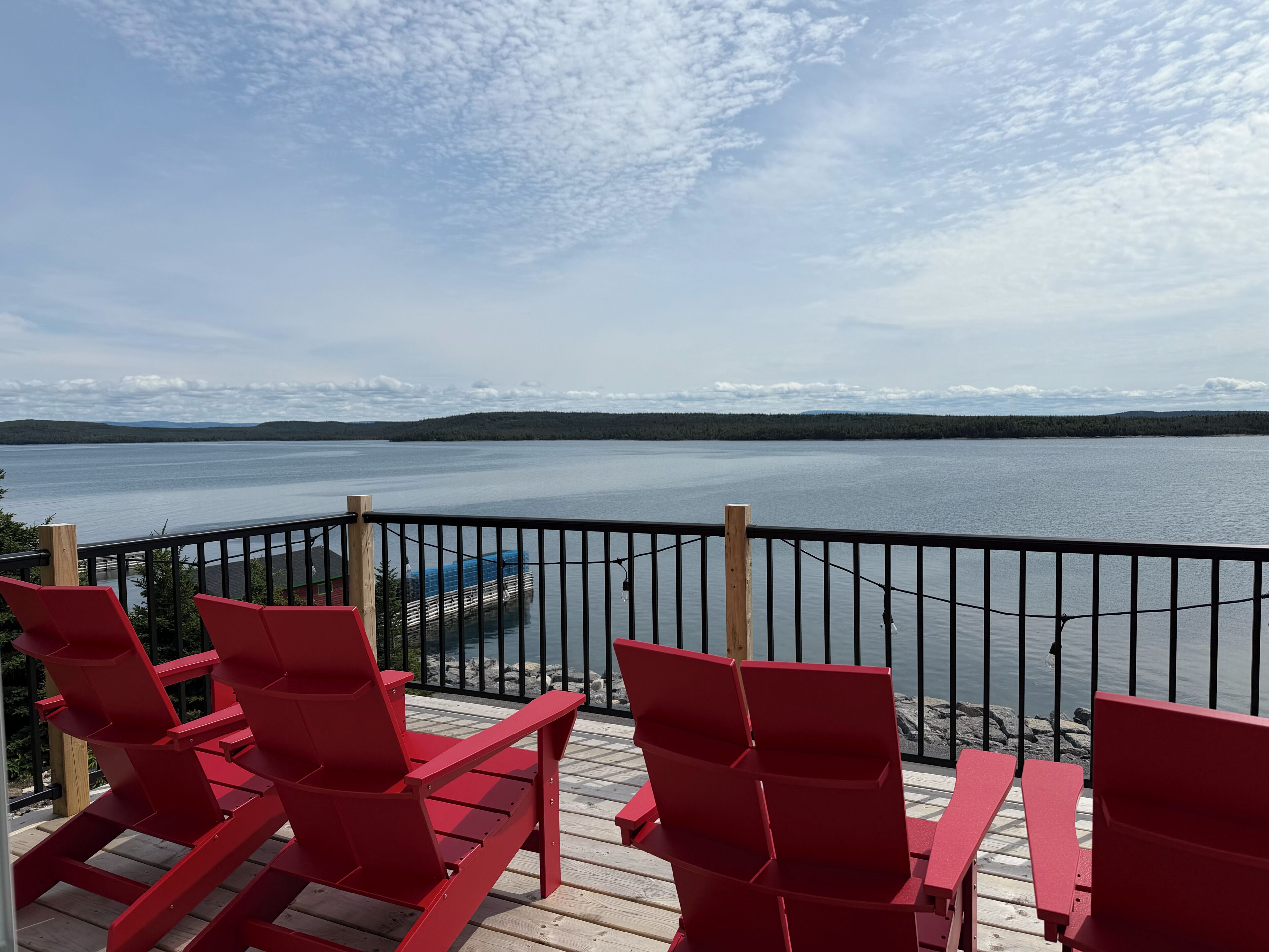 Une terrasse avec des chaises rouges et une table, donnant sur un lac paisible dont les rives sont bordées d’une forêt.