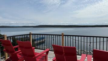 Une terrasse avec des chaises rouges et une table, donnant sur un lac paisible dont les rives sont bordées d’une forêt.