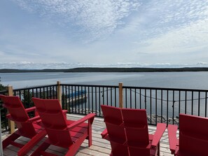 Une terrasse avec des chaises rouges et une table, donnant sur un lac paisible dont les rives sont bordées d’une forêt.