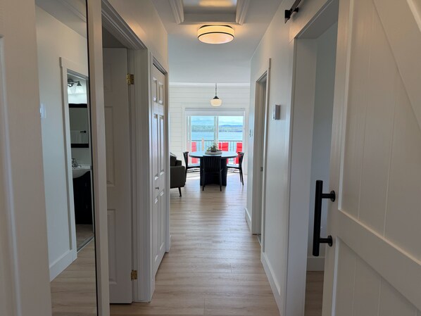 Un couloir aux portes blanches mène à une salle à manger qui offre une vue sur l’extérieur.