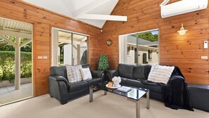 A modern living room with two black leather sofas, a glass coffee table, and a wooden wall with a large mirror.