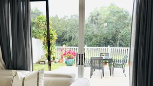 Ein Wohnzimmer mit einer Couch, einem Couchtisch mit Dekoration und Blick auf eine Terrasse mit Tisch und Stühlen.