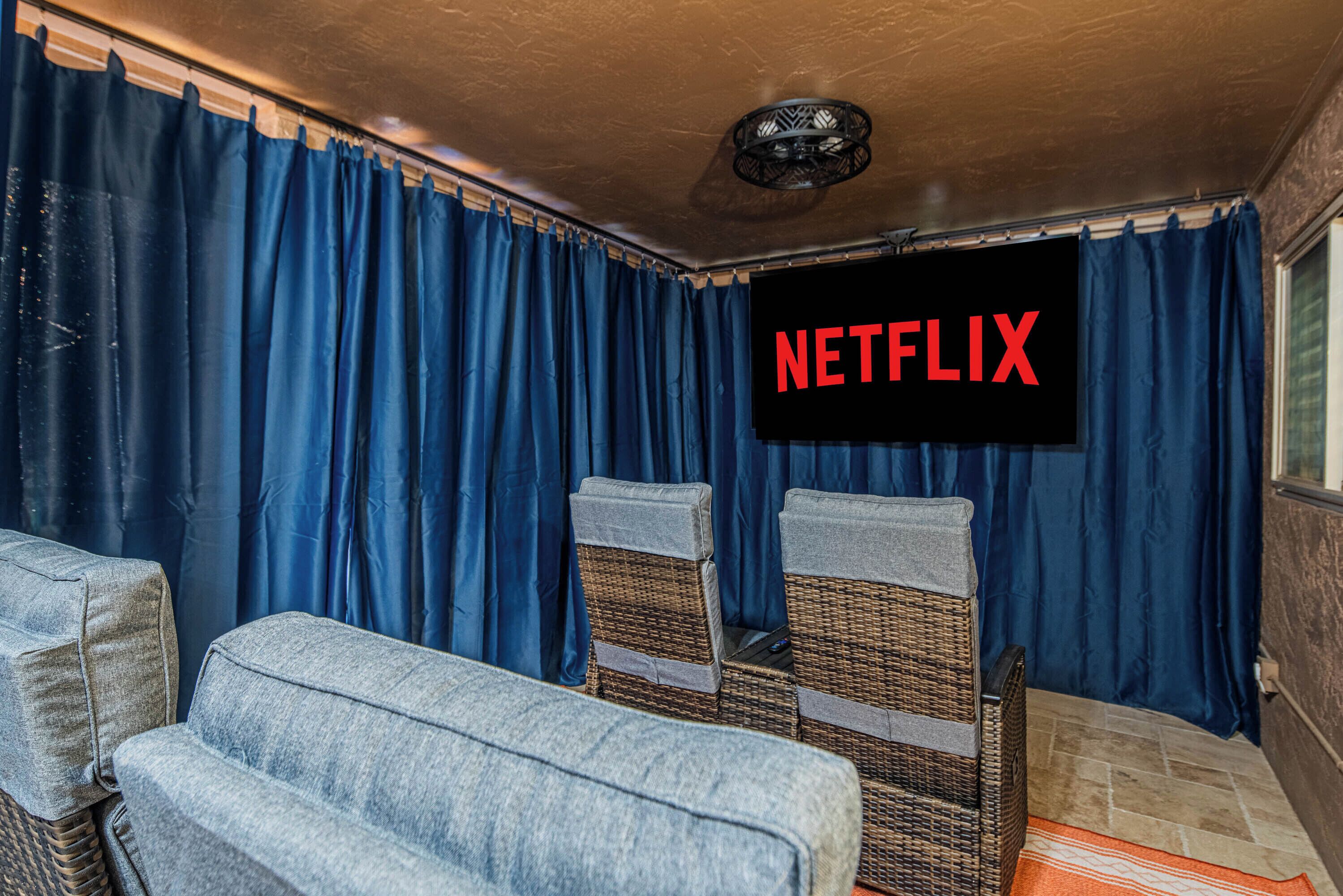 Une pièce avec des rideaux bleus, des chaises en osier et un écran de télévision affichant le logo « NETFLIX ».