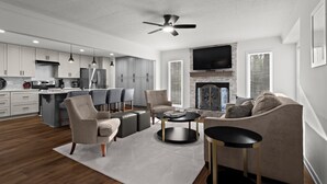 A modern kitchen with white cabinets, a dining area with grey chairs, a living room with a beige sofa and a coffee table, and a fireplace. - Chic & Comfy Stay • Close to Everything (Marietta)