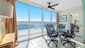 Ein Konferenzraum mit Glastisch, vier Bürostühlen, Deckenventilator und großem Fenster mit Blick auf einen Strand.