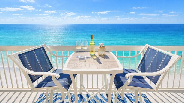 A balcony with two chairs and a table, overlooking a clear blue sea. - Beachfront 1BR + Bunks Condo w/ Pools Sleeps 6! (Panama City Beach)