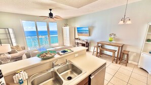 A modern kitchen with a large island, a dining area with wooden stools, and a view of the ocean through large windows. - Beachfront 1BR + Bunks Condo w/ Pools Sleeps 6! (Panama City Beach)