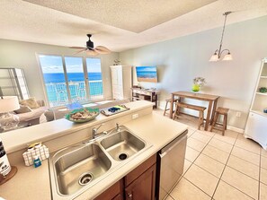 Una cucina moderna con una grande isola, una zona pranzo con sgabelli di legno e vista sull'oceano attraverso ampie finestre.