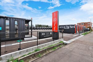 Un hotel llamado 'The Yard' con diseño moderno, que destaca un letrero vertical rojo prominente y una serie de contenedores negros y rojos.