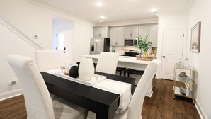 Une cuisine moderne avec des meubles blancs, des appareils en acier inoxydable et un coin repas comprenant une table noire et des chaises blanches.