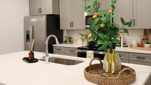 Une cuisine moderne avec des meubles gris, un réfrigérateur en acier inoxydable, un évier et une plante décorative ornée de citrons.