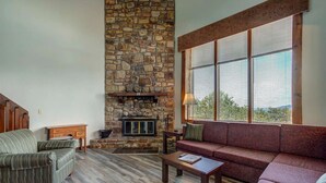 Ein Wohnzimmer mit Kamin aus Stein, einem großen Fenster mit Jalousien und einem roten Sofa.