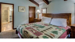 Ein Schlafzimmer mit einem großen Bett, Holzbalken an der Decke, einem Nachttisch und einer Tür zu einem weiteren Raum.