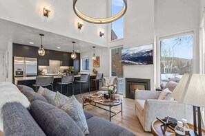 Un amplio salón con un sofá grande, una mesa de centro y una chimenea. Cuenta con una zona de cocina equipada con electrodomésticos modernos y taburetes de bar.