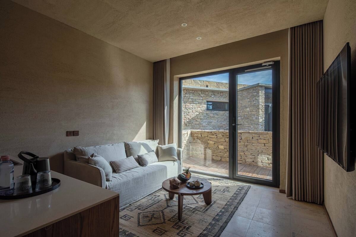 A modern living room with a sofa, coffee table, and a view of a stone building through a glass door.