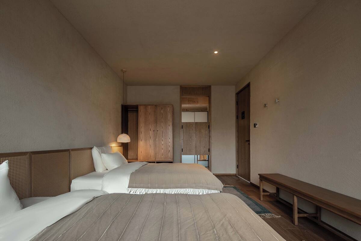A hotel room with two beds, a bench, and a wardrobe.
