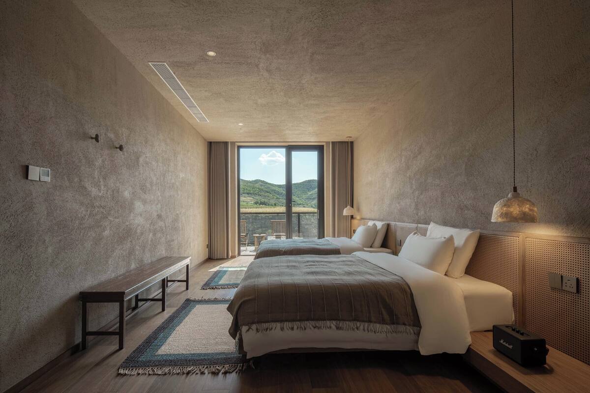 A bedroom with a large bed, a bench, and a view of the outdoors.