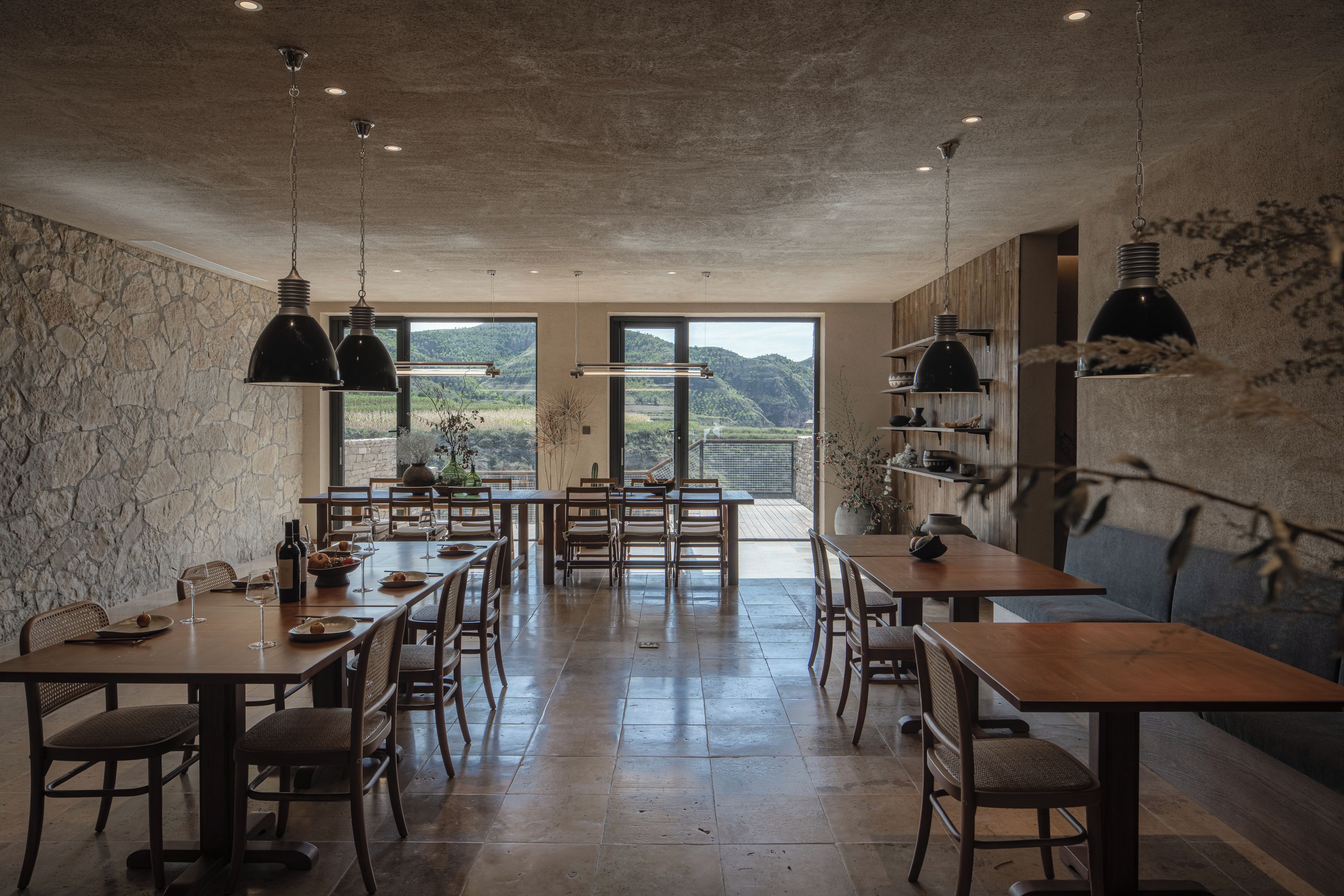 A dining area with a stone wall, wooden tables, and chairs, and a view of the outdoors.