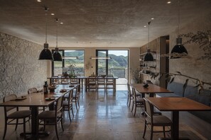 A dining area with a stone wall, wooden tables, and chairs, and a view of the outdoors.