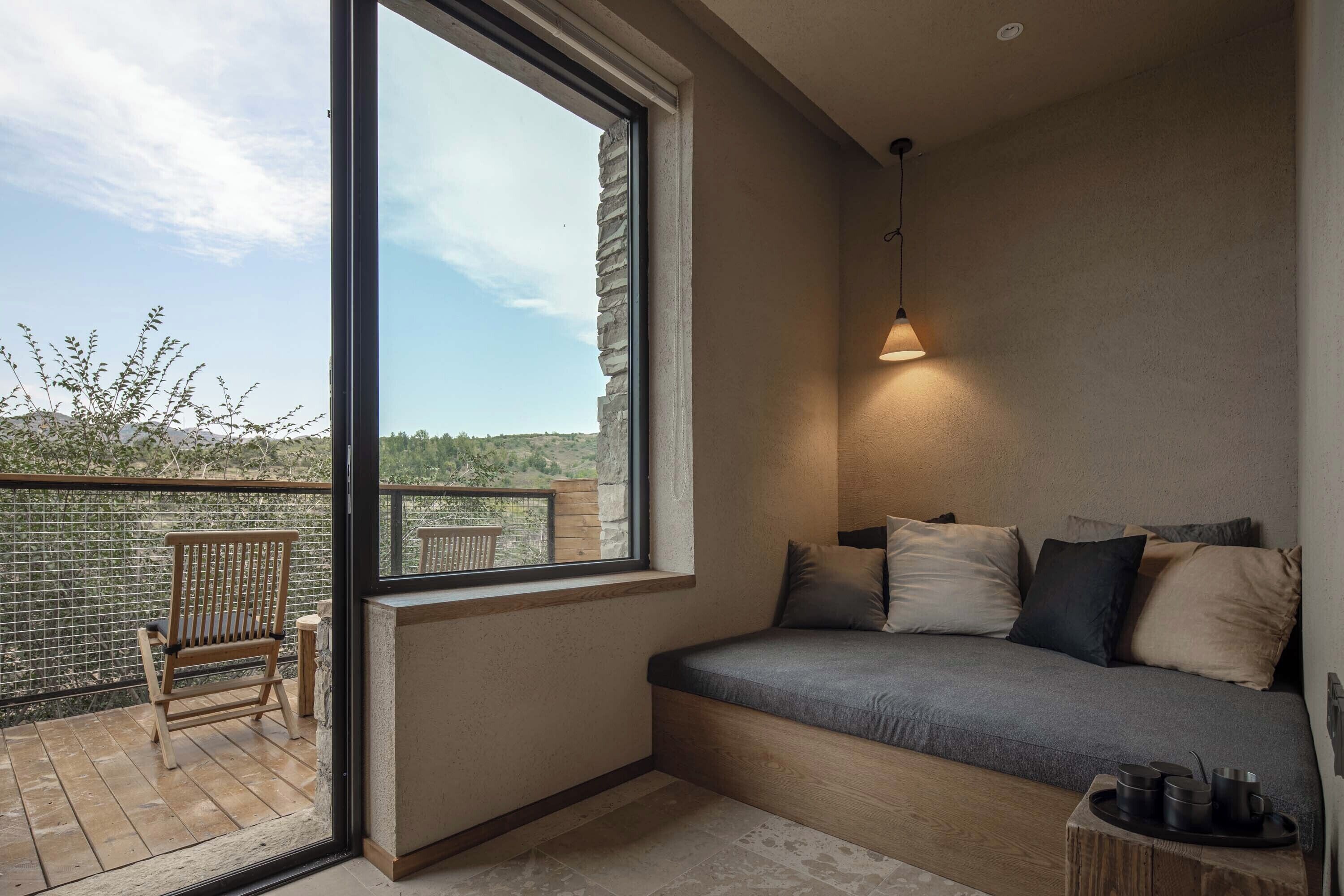 A balcony with a wooden chair, a cushioned bench, and a table with cups.