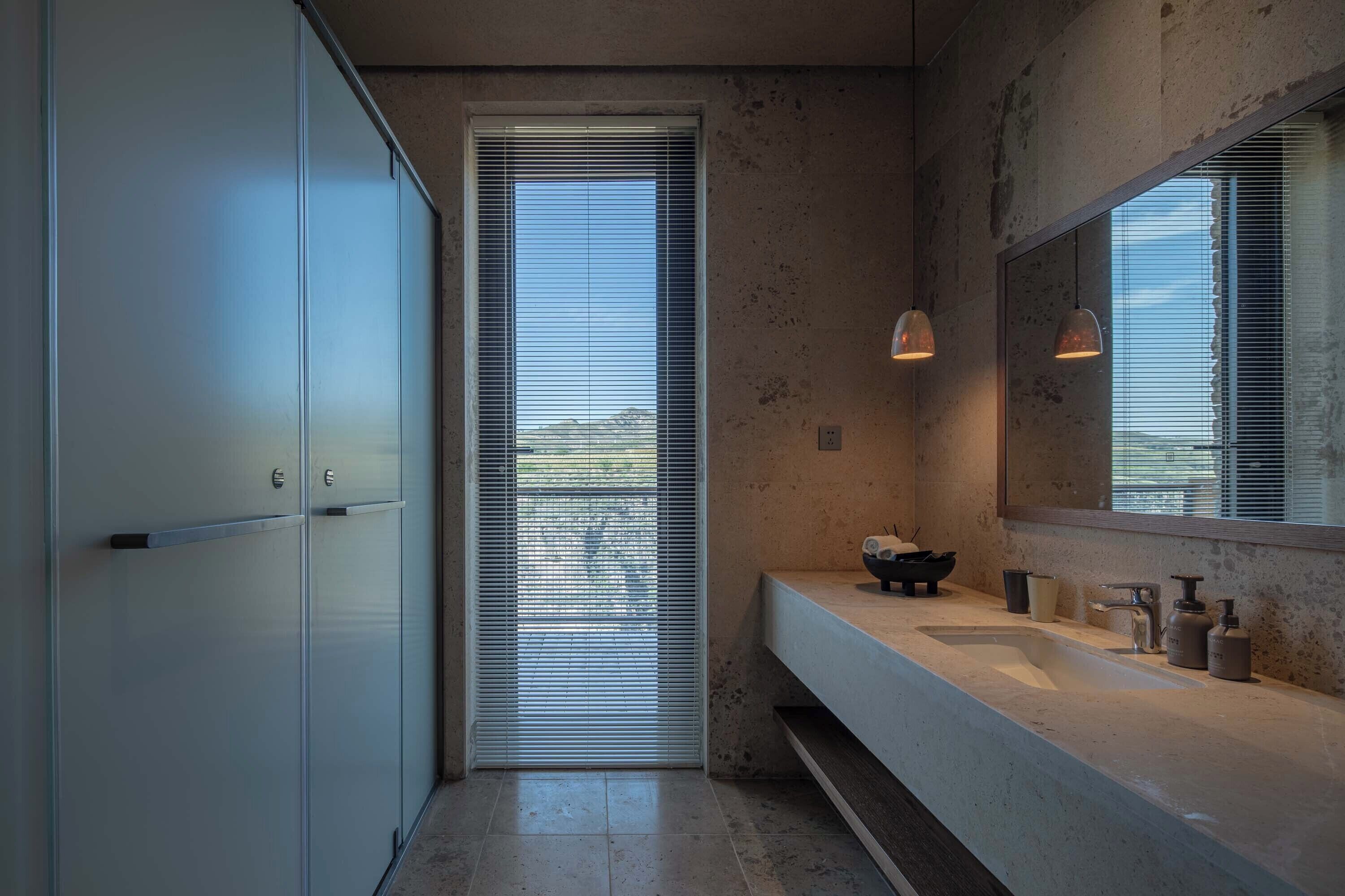 A modern bathroom with a large mirror, a sink, and a door with blinds.