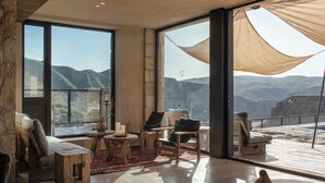 Un'ampia stanza con grandi finestre che si affacciano sulle montagne, un'accogliente area salotto con divano e poltrone, e un piccolo tavolino con candele.