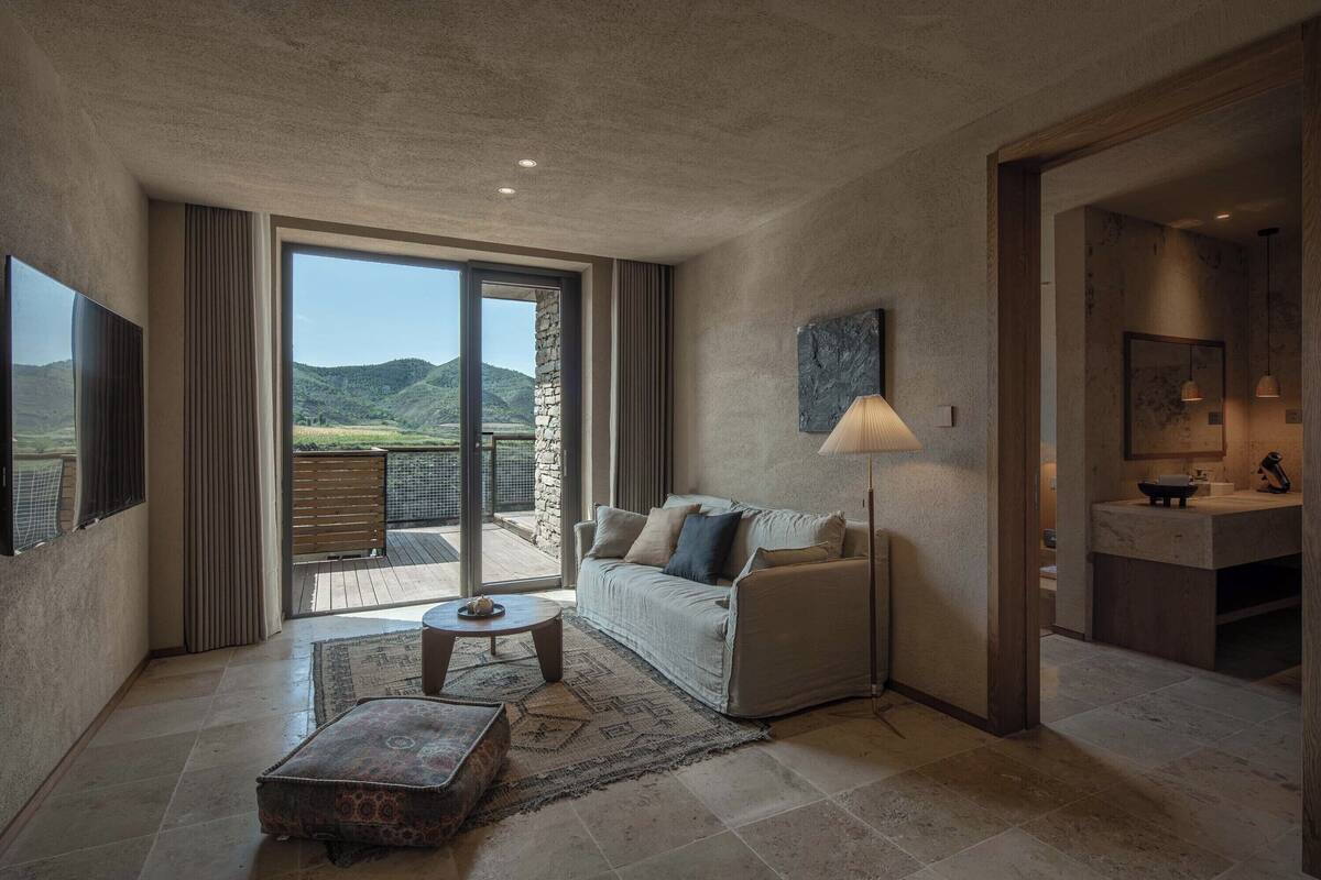A modern living room with a sofa, a coffee table, and a view of a mountainous landscape through large sliding doors.