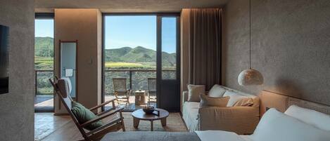 Una habitación moderna con una cama grande, un sofá y una mesa de comedor. Se ve una vista de montañas a través de amplios ventanales.