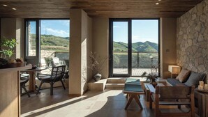Un ampio soggiorno con una grande finestra che offre vista su colline e una torre in lontananza. C'è un angolo salotto con divano e poltrone, un tavolino e una pianta in vaso.
