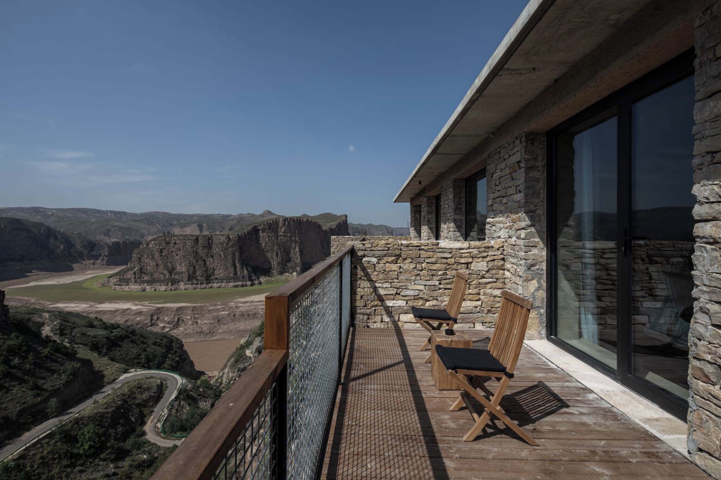 A balcony with a stone wall, two wooden chairs, and a view of a canyon.