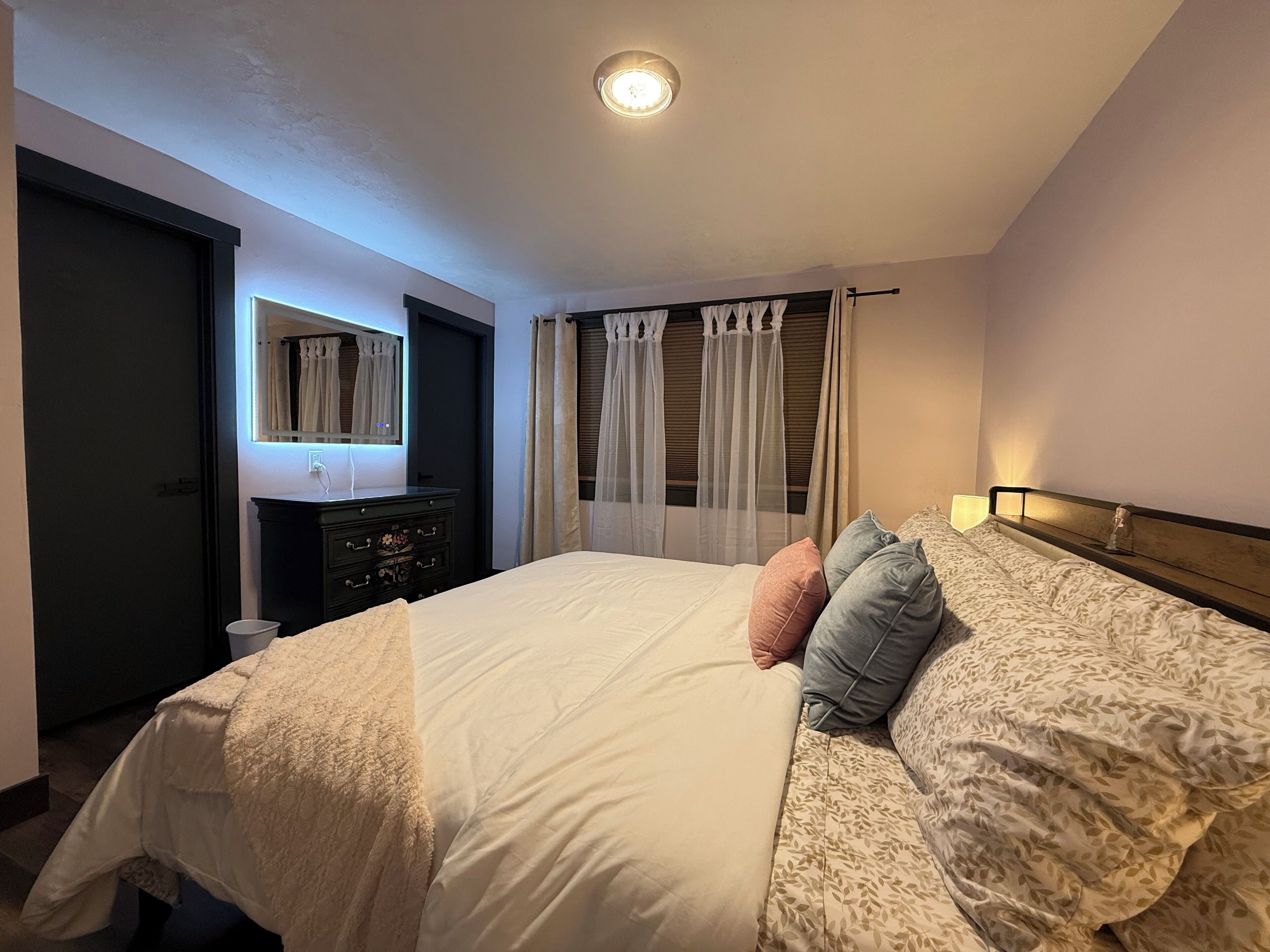 A bedroom with a bed, a dresser, a mirror, and a window with curtains.