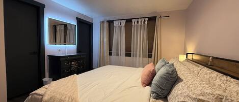 A bedroom with a bed, a dresser, a mirror, and a window with curtains.