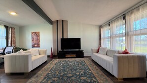 A living room with two white sofas, a large flat-screen TV, a patterned rug, and a tall striped wall panel. - Updated 3BR Home – Quiet, Comfortable Stay with Luxury Master & Spa Shower (Kennewick)
