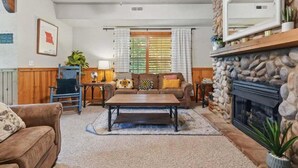 A cozy living room with a fireplace, a sofa, a coffee table, and a wooden chair. - Close to Shows, Dining & Golf • 2BR + Loft Cabin (Branson)