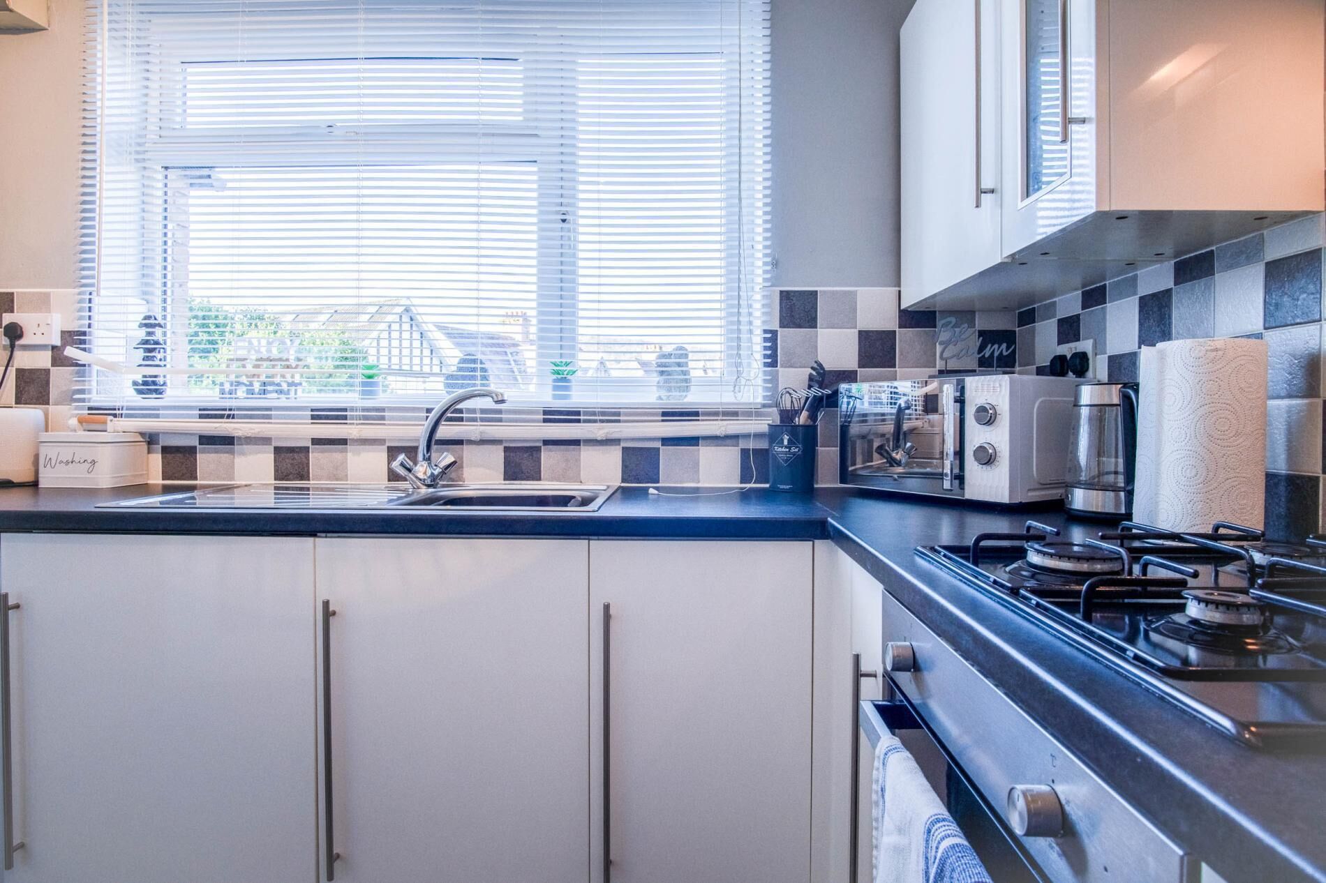 A modern kitchen with a checkered backsplash, a built-in oven, a gas stove, and a window with blinds.